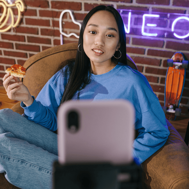 uma jovem da geração alfa sentada no sofá olhando para um celular que está no tripé