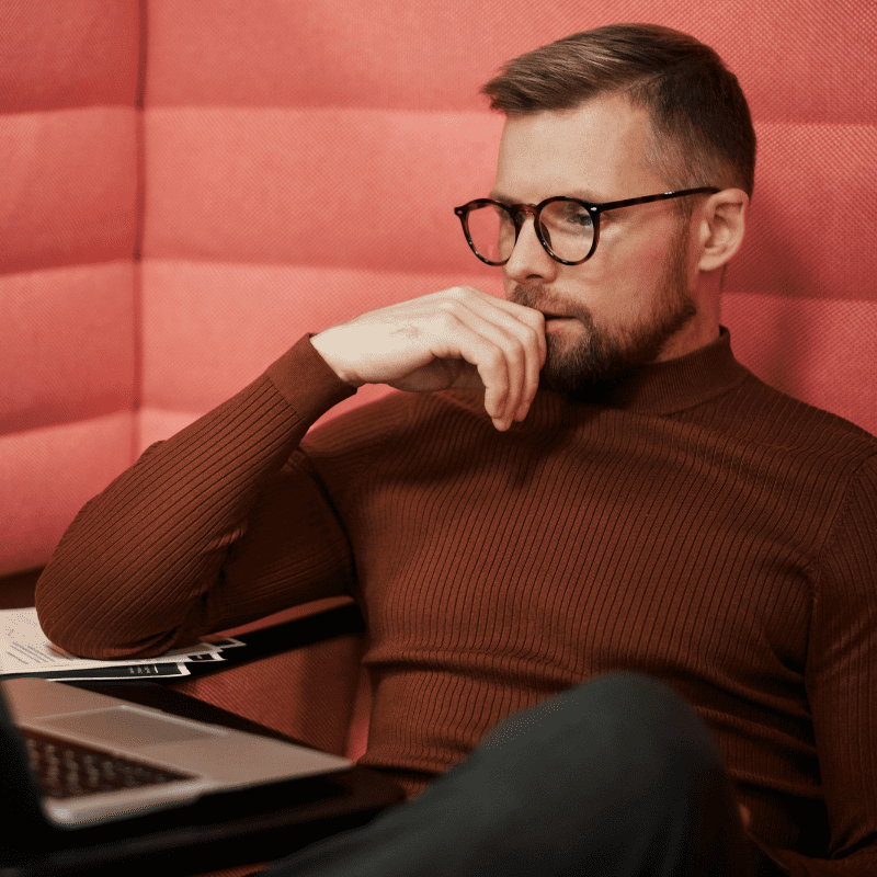um homem sentado no sofá olhando pensativo para o notebook